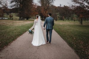 Bride and groom hand in hand waking away from the camera. The surrounding park is vast and empty.