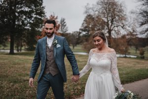 Bride and groom walking happily hand in hand with a vast park in background.