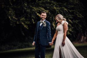 Bride and groom walking hand in hand. The bride is looking at th floor the groom is smiling at the bride.