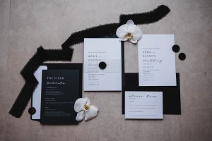 Wedding stationery laid out in a creative pattern. Black and white theme with black ribbon and Orchids. Taken from above toshowcase wedding trends 2023.