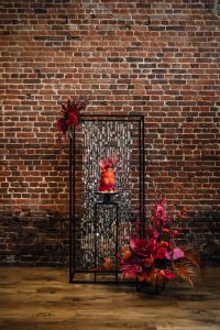 Bright orange and pink wedding cake on a black metal display frame with silver sparkles behind. 