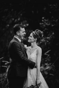 Bride and groom holding each other in an embrace. The groom is laughing and the bride is facing him smiling.