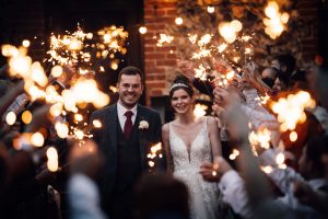 Bride and groom facing the camera smiling. They are surrounded by a tunnel of their guests holding sparklers.