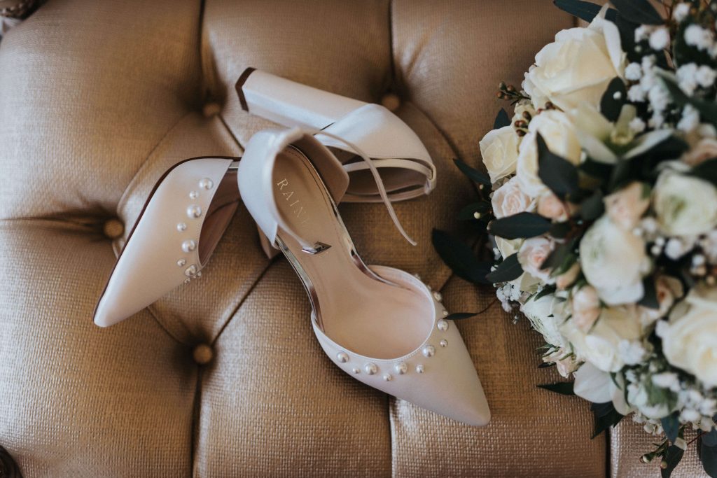 Bridal shoes sitting on gold padded seat with bridal bouquet to the right. Taken at Holmewood Hall wedding Venue.