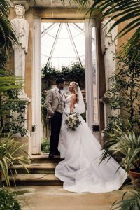 Bride and groom Kissing in the conservatory at Harlaxton Manor wedding venue. They are surrounded by green Leaves and plants.