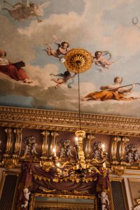 Painted ceiling at Harlaxton Manor. Blue sky filled with cherubs, gold mouldings and gold chandelier.