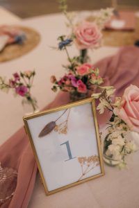 Venue decor at Crown Hall farm, Wedding venue Lincolnshire. The table has a number 1 in a gold frame and 3 small vases of flowers in pinks and blues.
