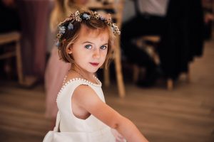 A young brides maid portrait she looks directly to the camera. She has a floral crown and deep blue eyes wearing a white dress.