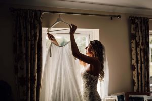 Bride reaching up to get her wedding dress down from a hanger. She is back lit and slightly in shadow. Used to show the power of story telling at weddings.