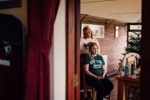 Colour image of a blonde woman getting her hair curled for a Christmas wedding in Oakham. She is wearing a green t-shirt and black trousers.