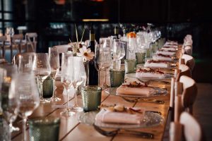 table set up at Sandon Manor. Long wooden tables with green glasses, glass plate chargers and flowers.