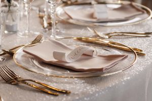 Gold and glass plate with pink napkin and white scroll name card. Set up for a wedding.