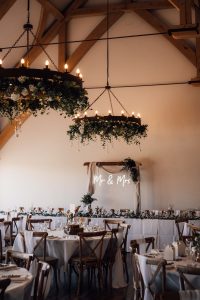 Portrait image of sissons barn with chandelier hanging covered in greenery. A neon sign saying Mr and Mrs is in the background.